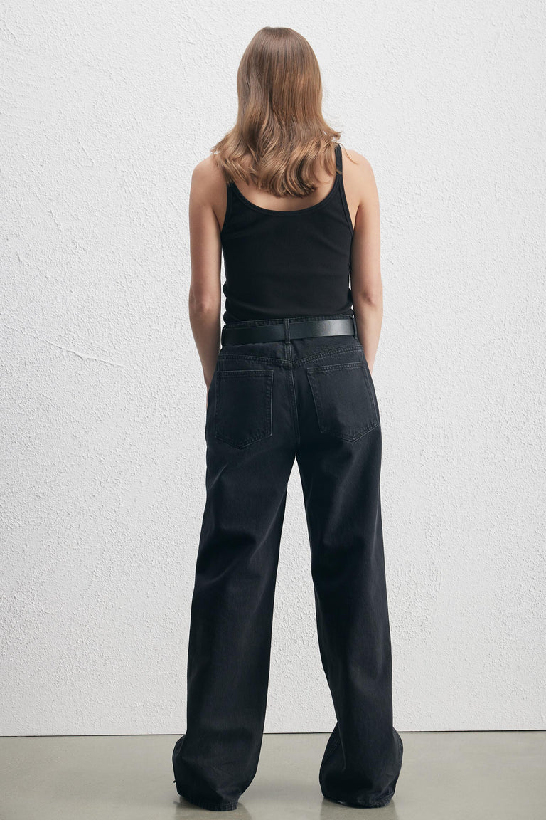Woman wearing black ribbed tank top paired with relaxed black denim jeans and a black belt, back view