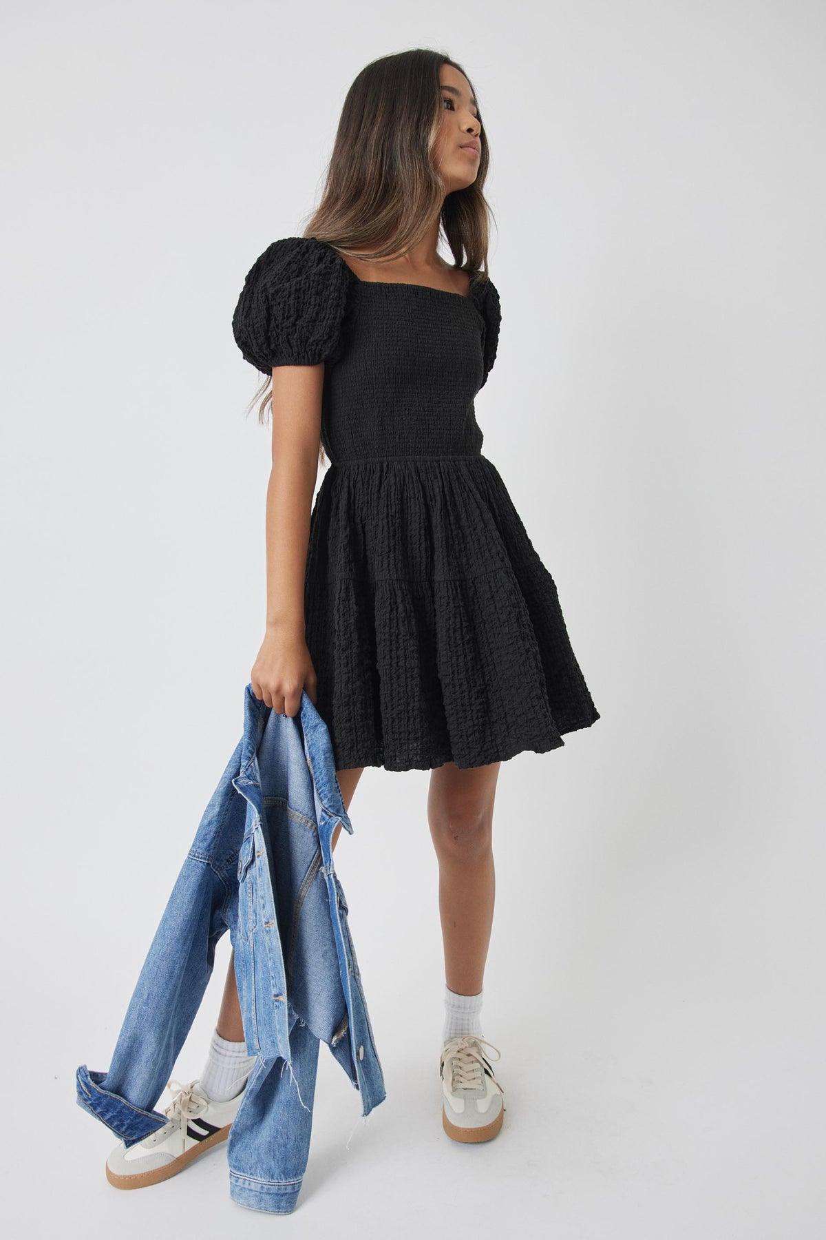 Side view of girl wearing black Girls Maude Mini Dress holding denim jacket by Decjuba Australian fashion brand