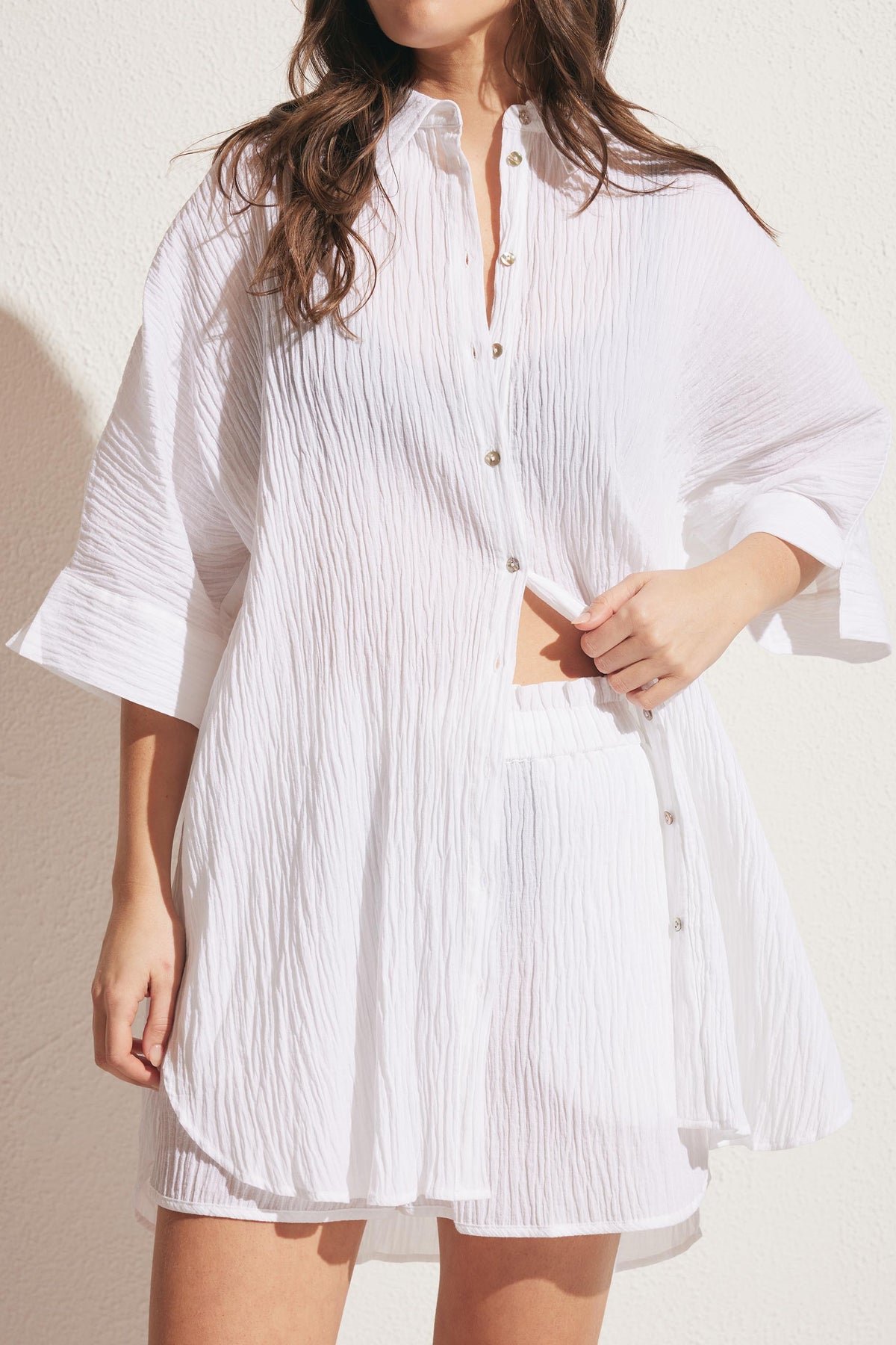 Woman wearing a lightweight white crinkle fabric shirt with three-quarter sleeves styled casually over matching shorts