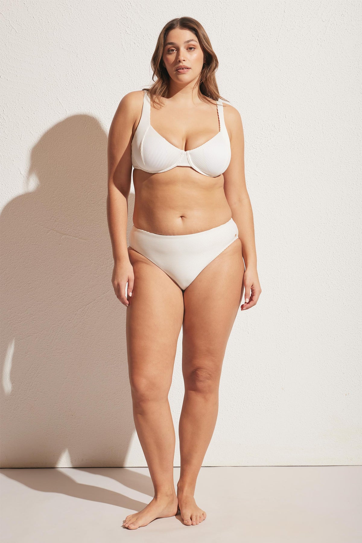 Woman wearing an off-white ribbed bikini bottom paired with a supportive underwire bikini top in soft natural light