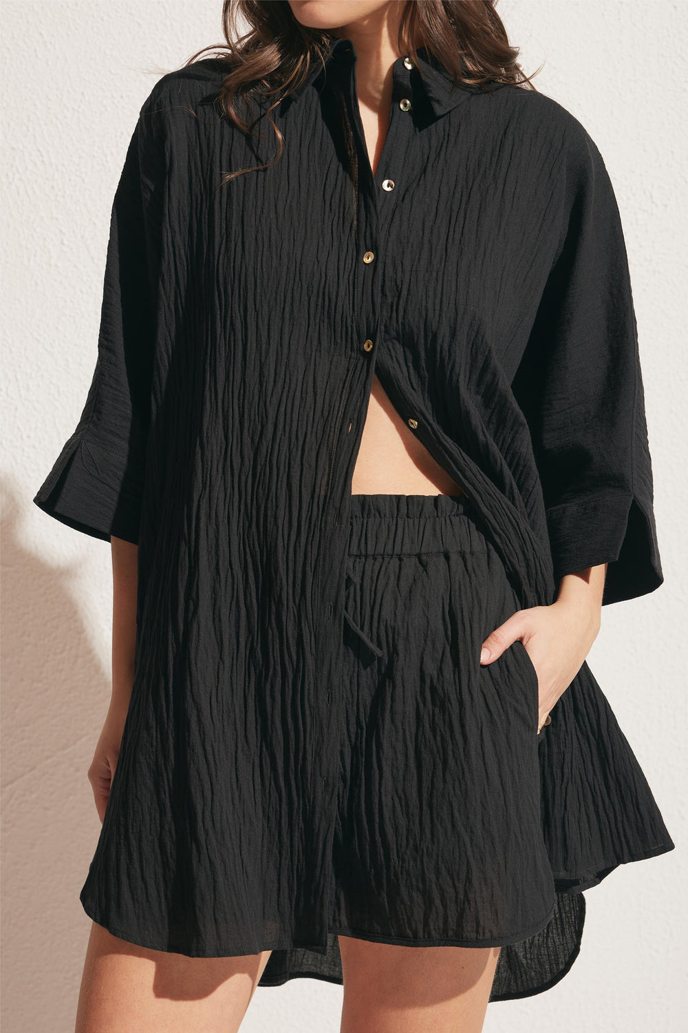 Woman wearing textured black relaxed shorts paired with a loose button-up shirt, styled with a casual hand-in-pocket look