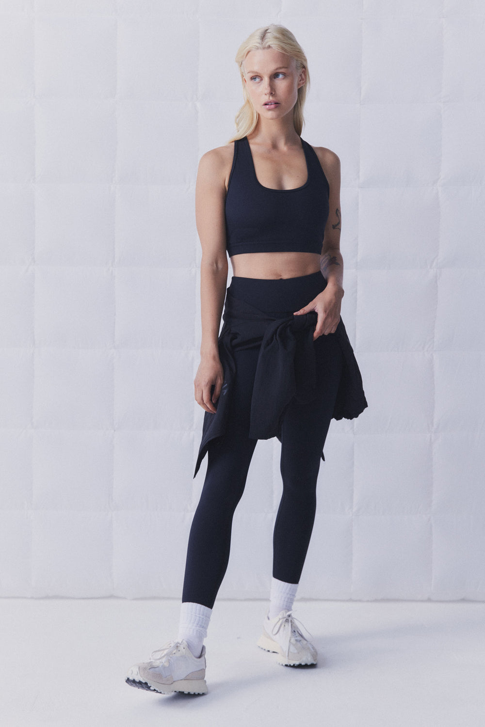 Woman wearing a black racerback sports bra, leggings and sneakers in a studio