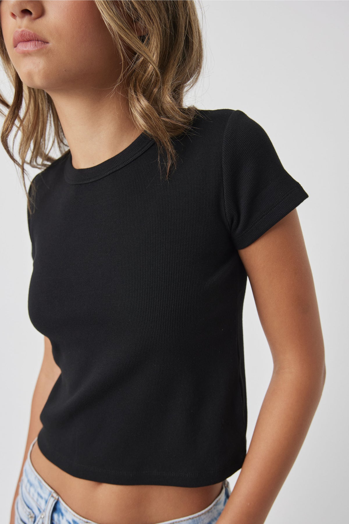 Girl wearing Girls Harper Crop Tee in black ribbed fabric styled casually with light denim by DECJUBA Australian fashion brand