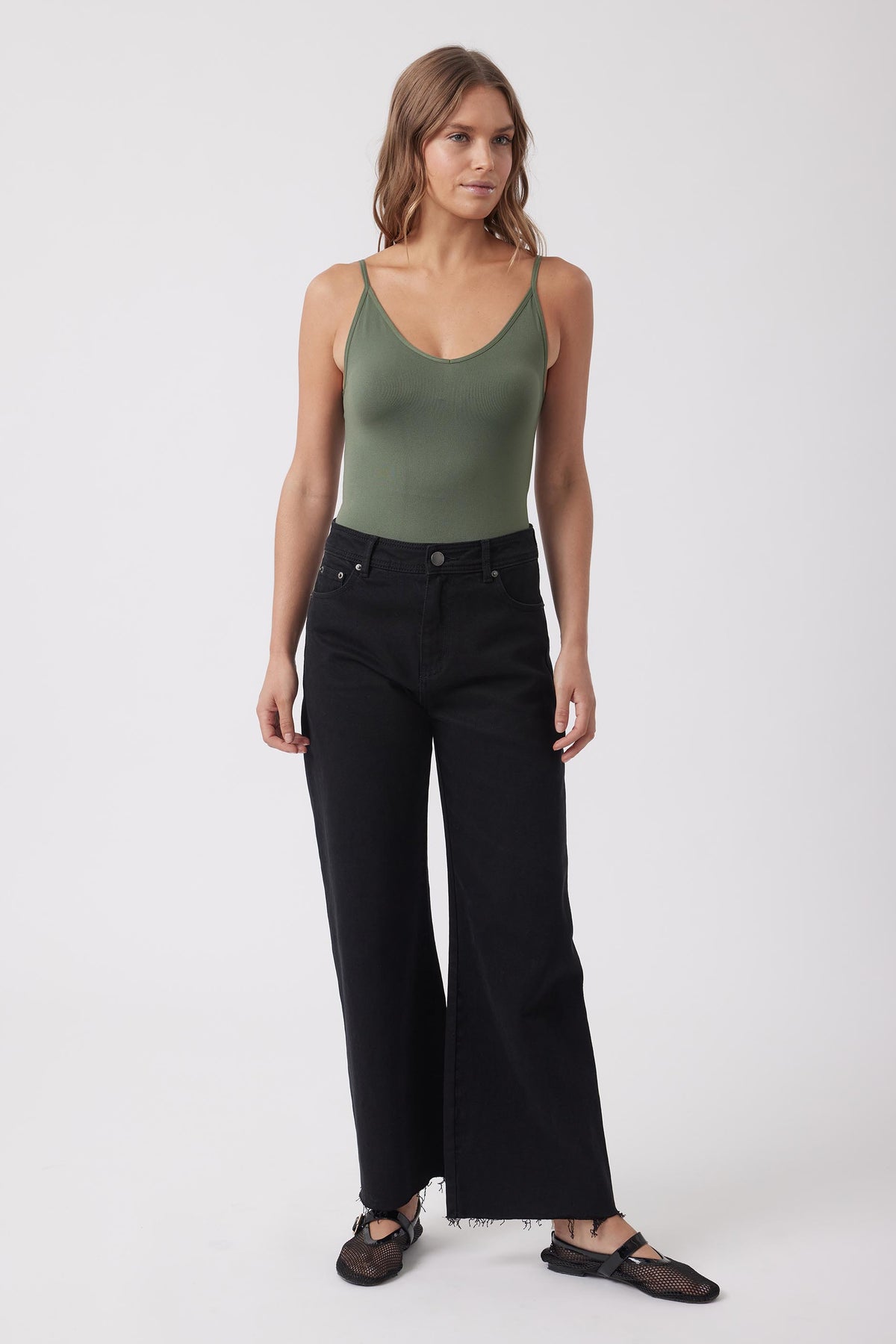 Woman wearing an olive green fitted V neck tank top with black wide leg jeans and flat shoes