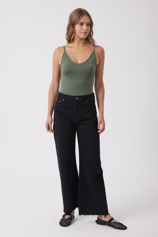 Woman wearing an olive green fitted V neck tank top with black wide leg jeans and flat shoes
