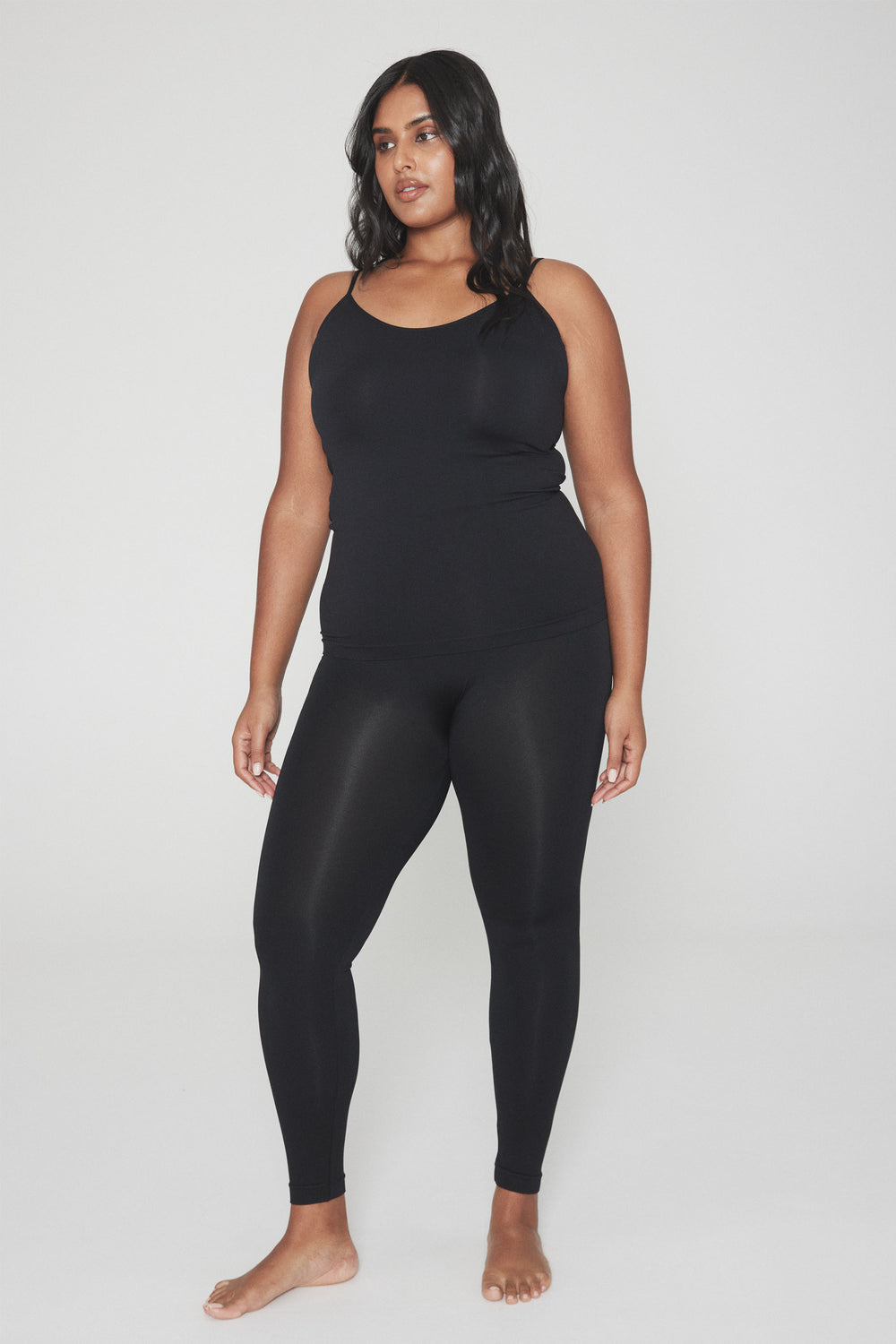 Woman wearing sleek black seamless leggings paired with a fitted black tank top in a relaxed pose