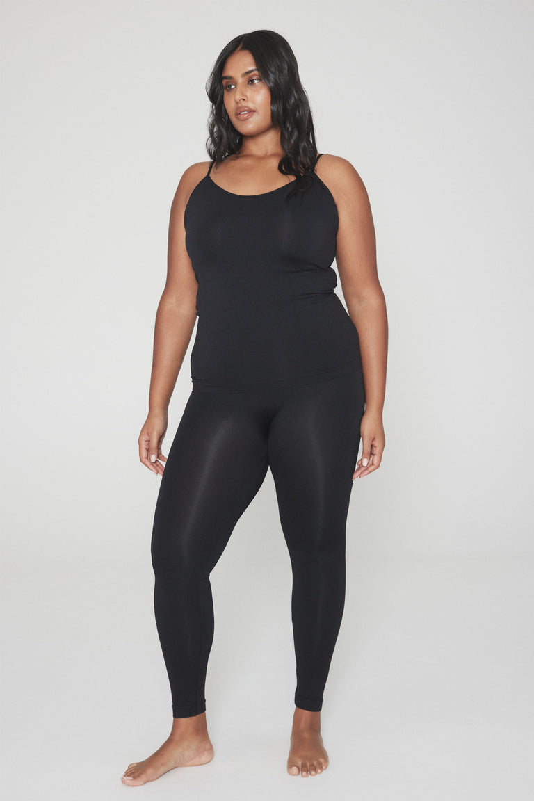 Woman wearing sleek black seamless leggings paired with a fitted black tank top in a relaxed pose
