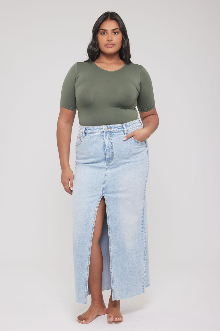 Woman wearing an olive fitted short sleeve tee paired with a light blue high-waisted denim skirt with front slit.