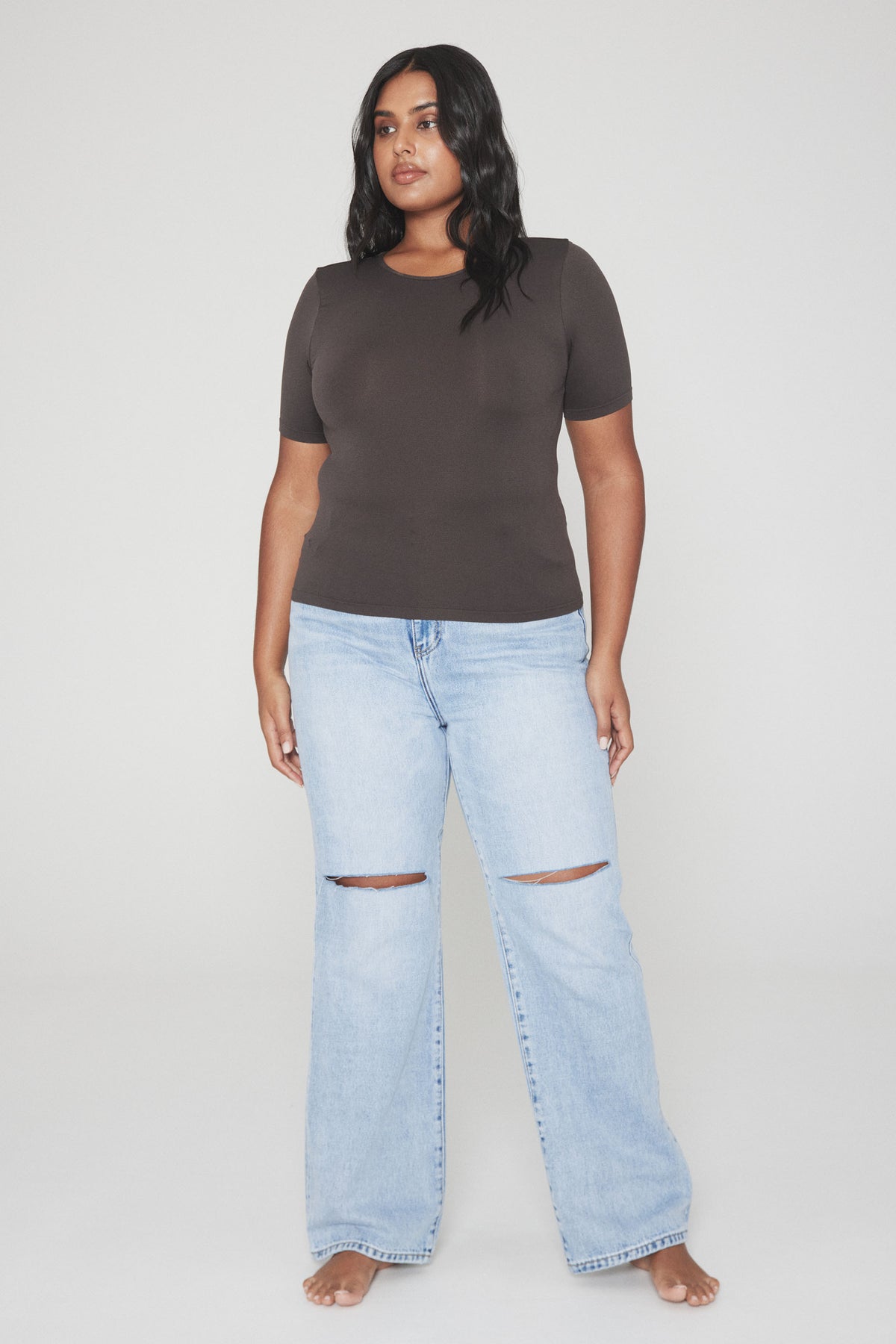 Woman wearing a fitted dark brown crew neck tee with light blue wide leg ripped jeans