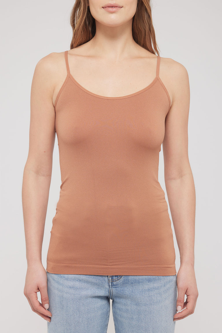 Woman wearing a fitted tan seamless thin strap tank with a scoop neckline and jeans