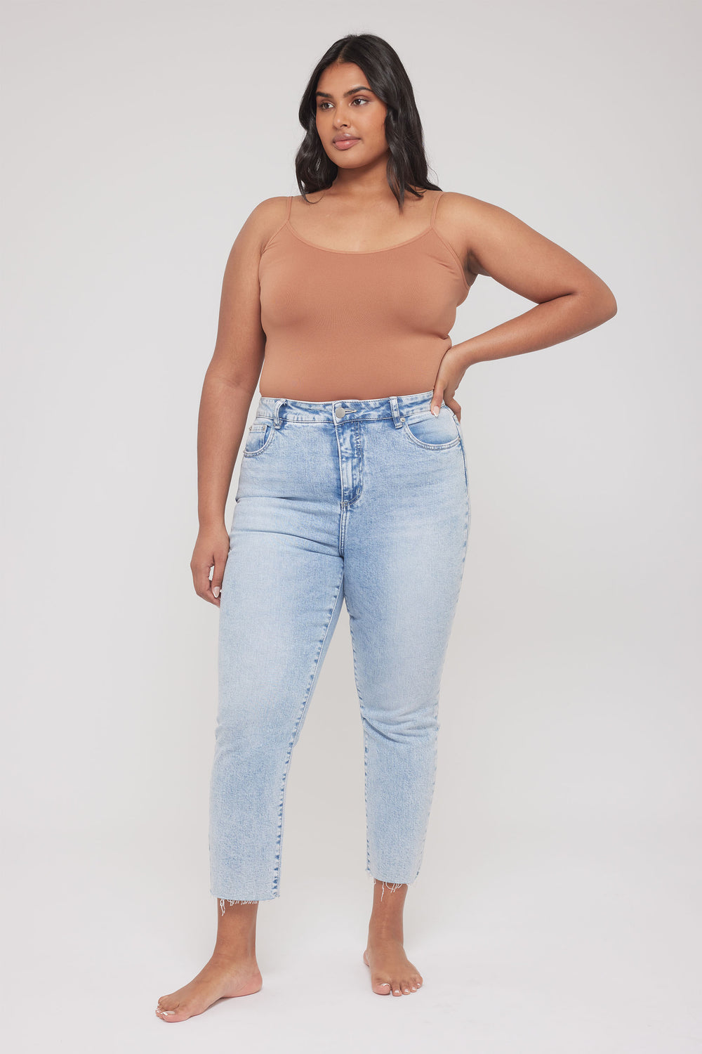 Woman wearing a tan fitted thin strap tank with light blue jeans