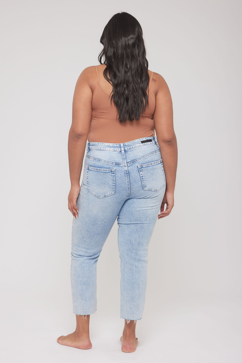 Back view of a woman wearing a fitted brown thin strap tank with light wash jeans