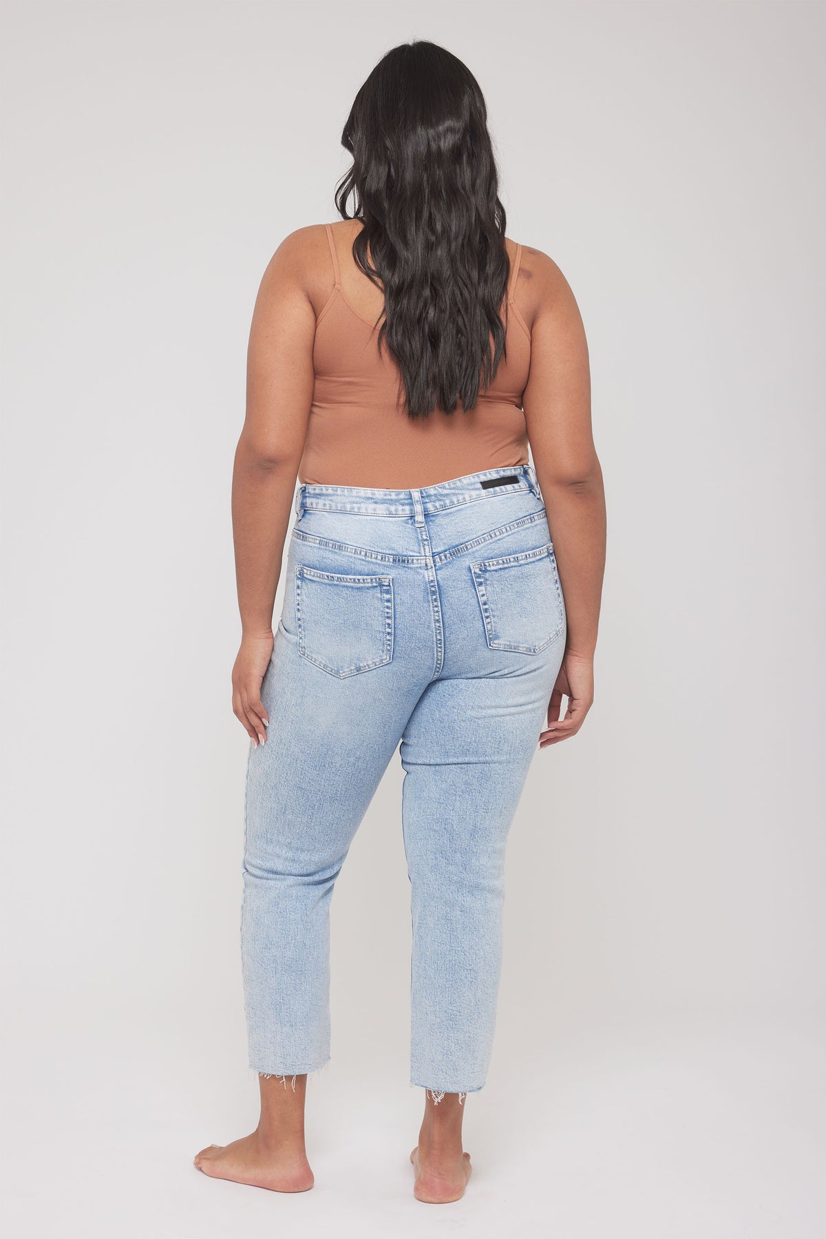 Back view of a woman wearing a fitted brown thin strap tank with light wash jeans