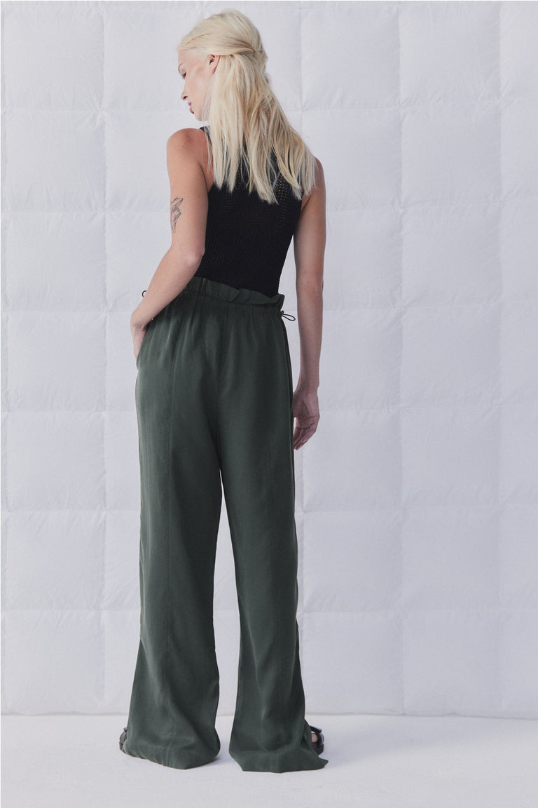 Woman viewed from behind wearing dark green high rise wide leg pants with an elasticated toggle waist and full length fit