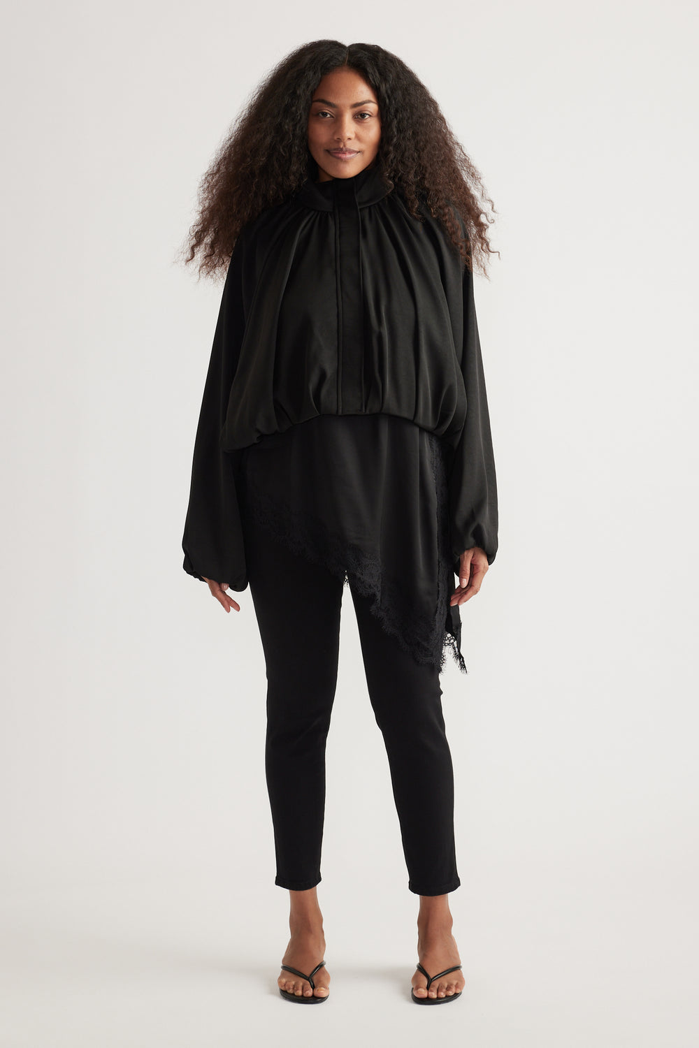 Woman wearing black high rise ankle-length skinny jeans with a flowing black blouse and strappy sandals
