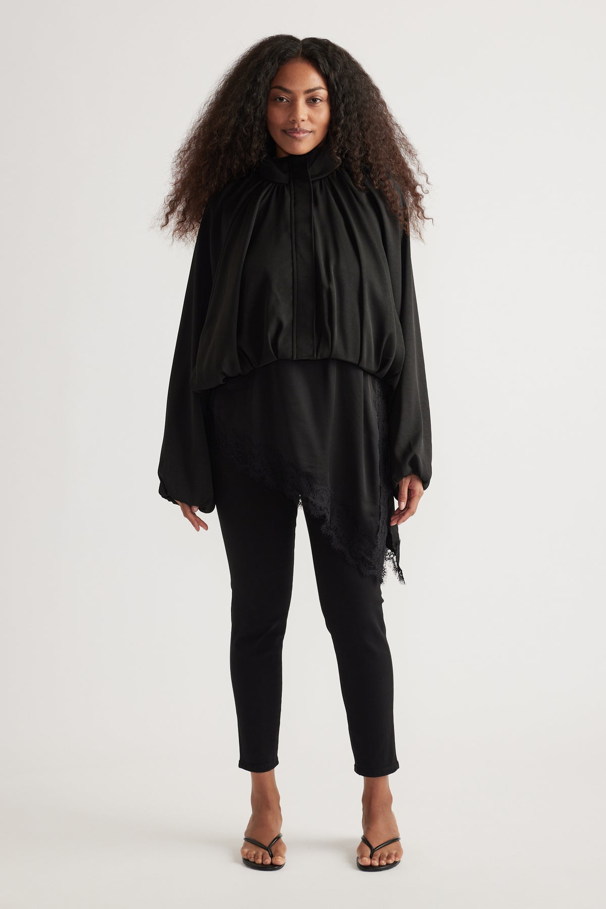 Woman wearing black high rise ankle-length skinny jeans with a flowing black blouse and strappy sandals