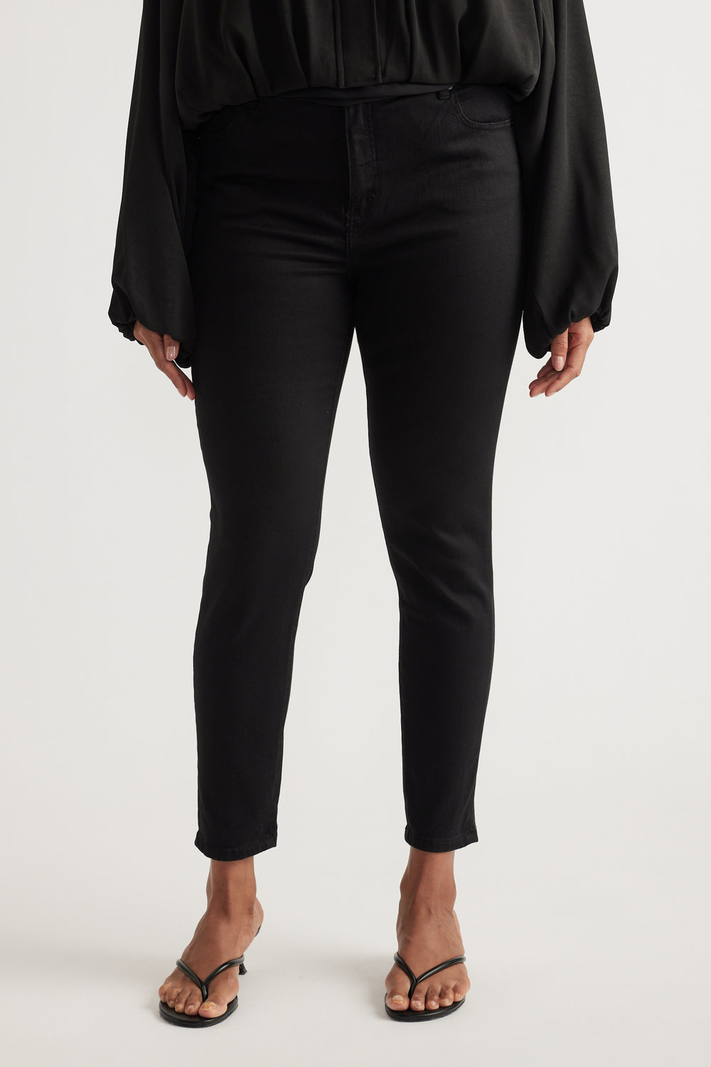 Woman wearing black high-rise skinny ankle jeans with a black blouse and strappy sandals