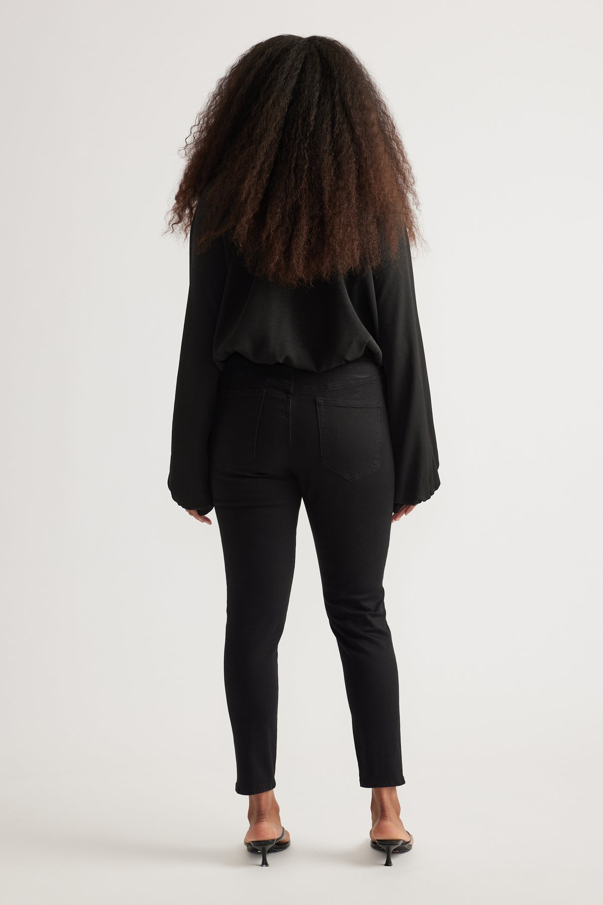 Back view of woman wearing black high rise skinny jeans with ankle length fit and a black long sleeve top
