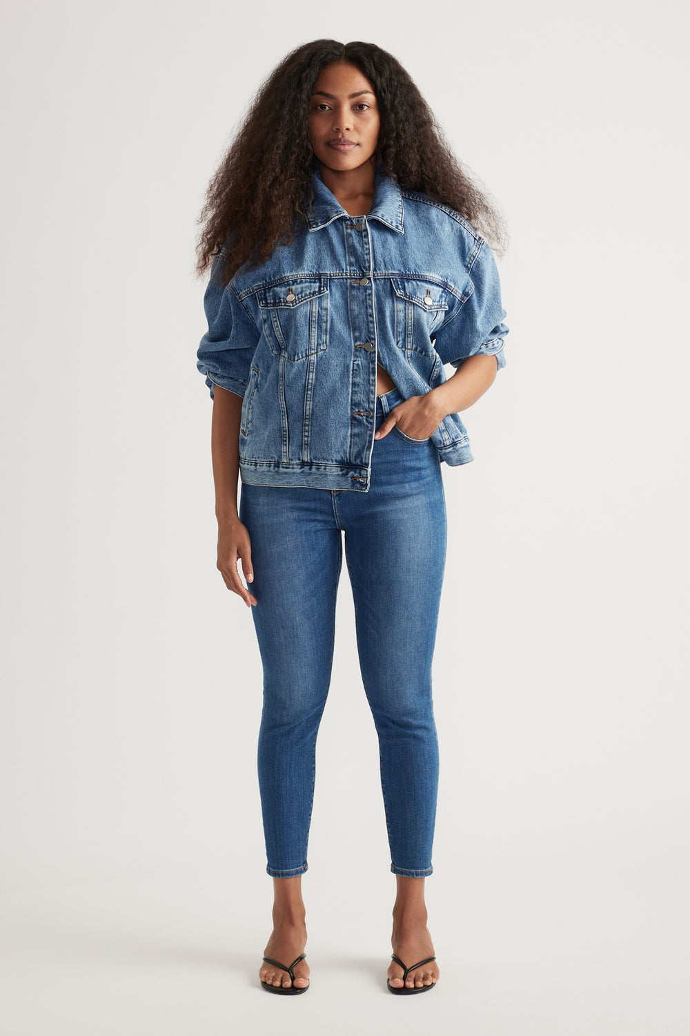 Woman wearing blue high rise skinny jeans with a relaxed denim jacket and strappy sandals
