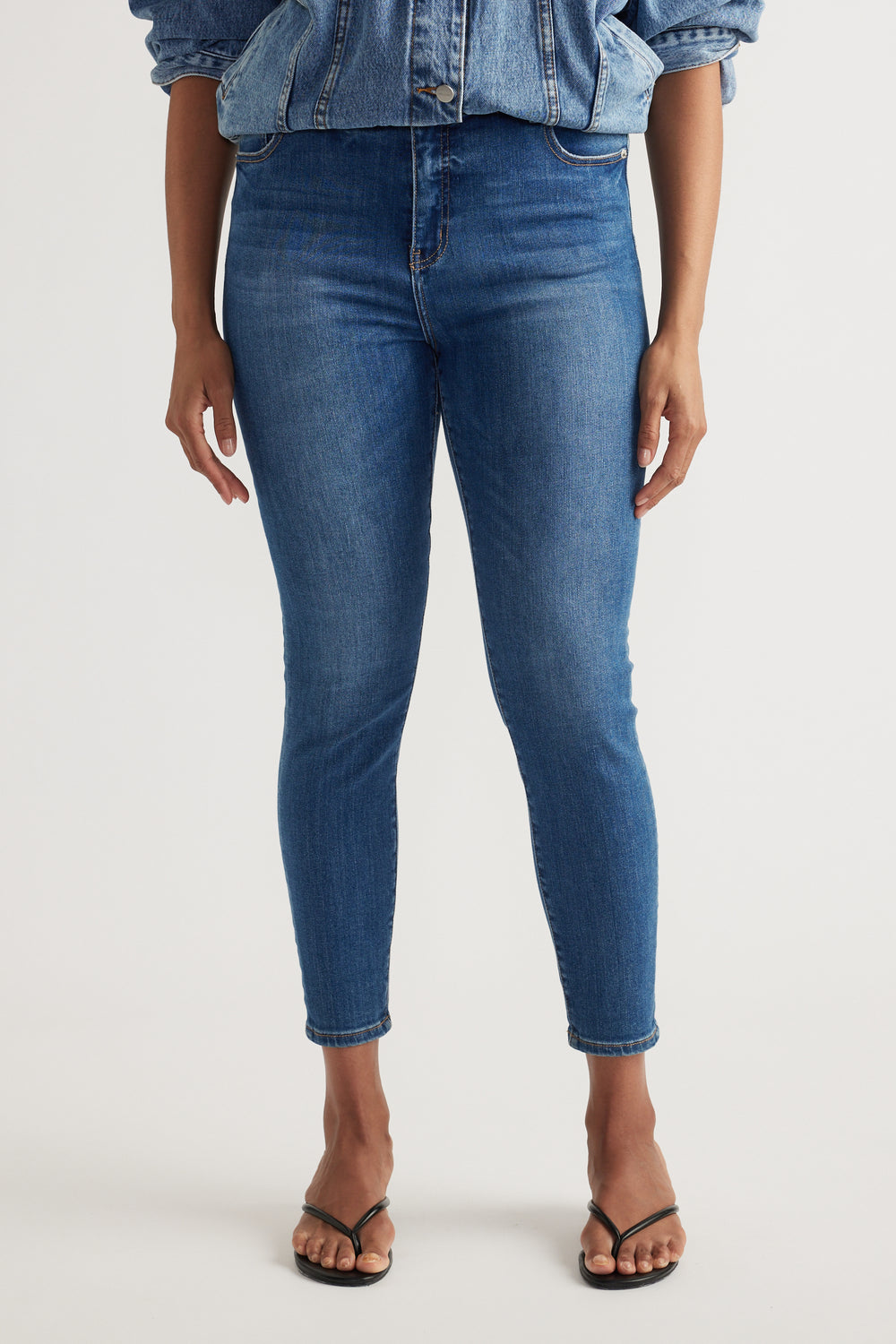 Woman wearing high rise blue skinny jeans with ankle-length hems and a denim jacket