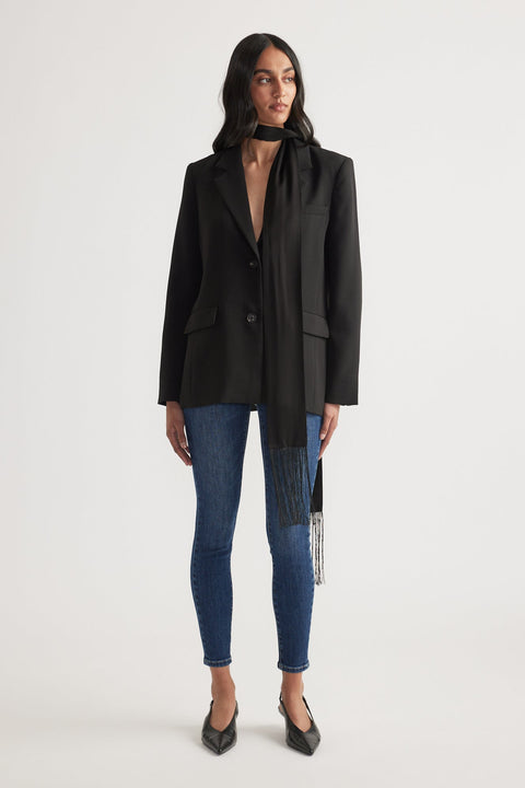 Woman wearing a black tailored blazer with long scarf paired with dark blue high rise skinny jeans and black pointed heels