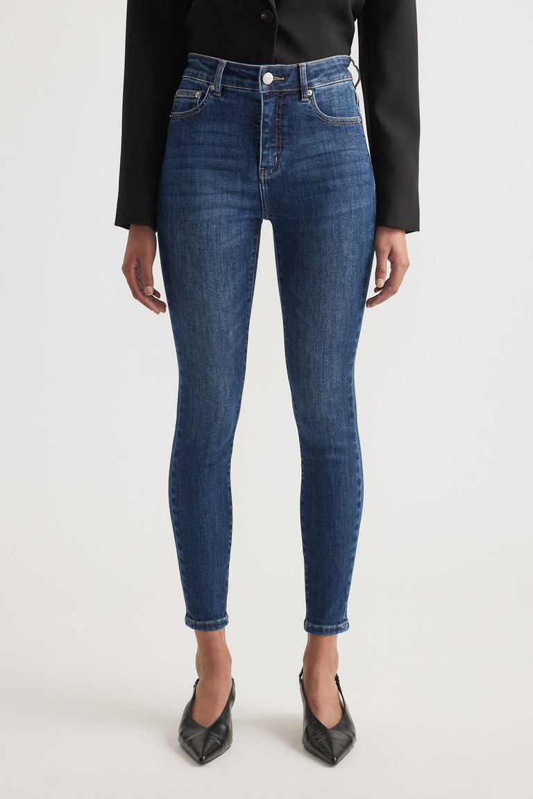 Woman wearing mid-blue high rise skinny jeans paired with a black blazer and pointed black heels
