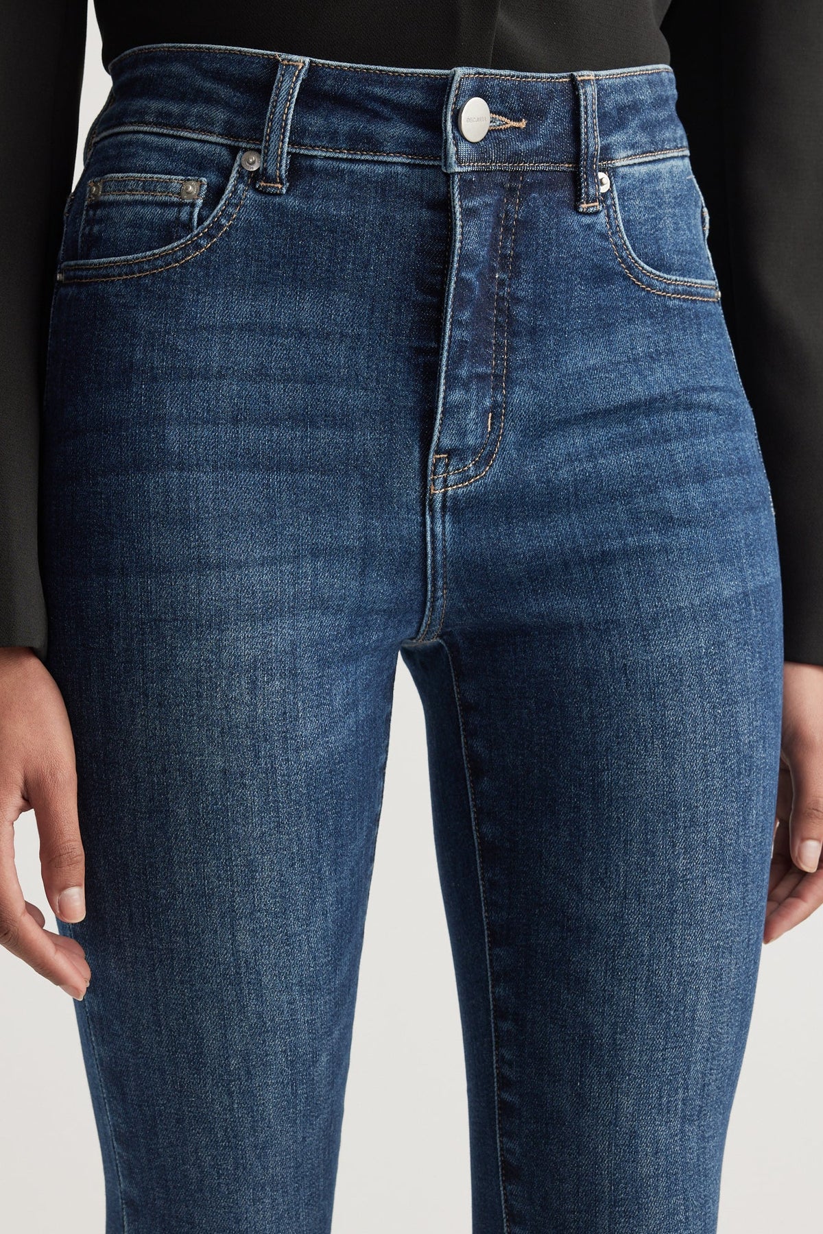 Close-up of dark blue high rise skinny jeans with subtle fading and contrast stitching worn with a black top