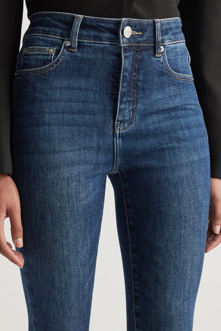 Close-up of dark blue high rise skinny jeans with subtle fading and contrast stitching worn with a black top
