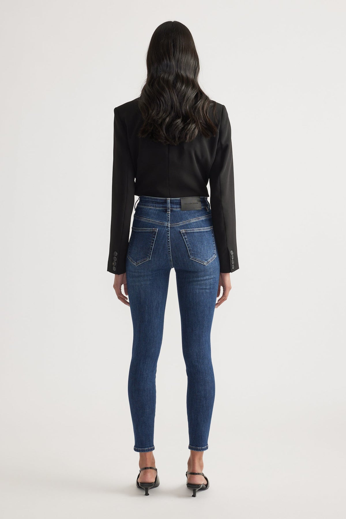 Woman wearing dark blue high rise skinny jeans paired with a fitted black blazer and black heeled sandals