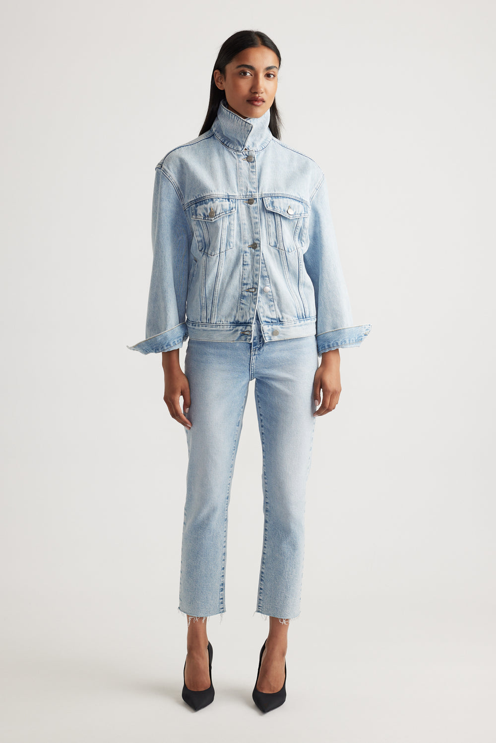 Woman wearing a light blue denim jacket and cropped straight jeans on a white background