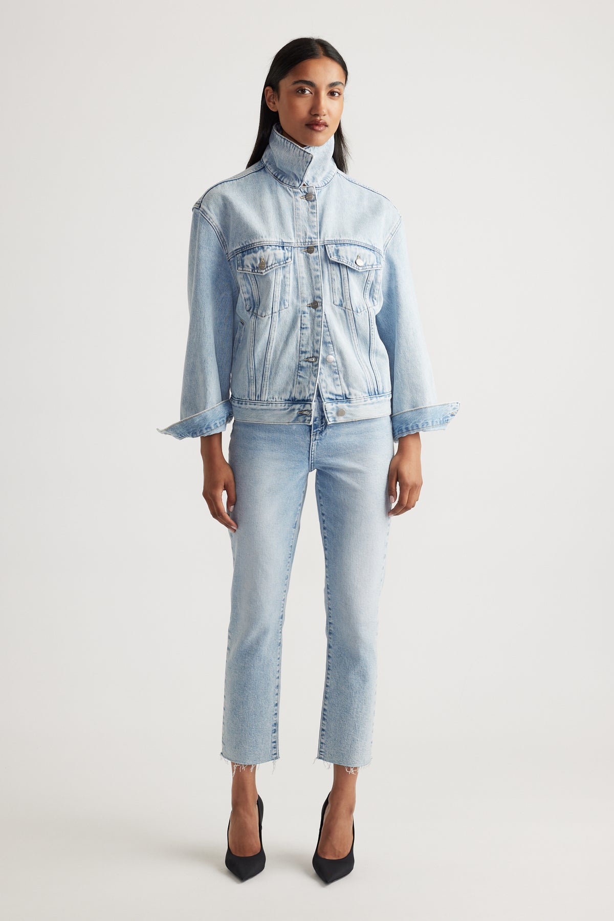 Woman wearing a light blue denim jacket and cropped straight jeans on a white background