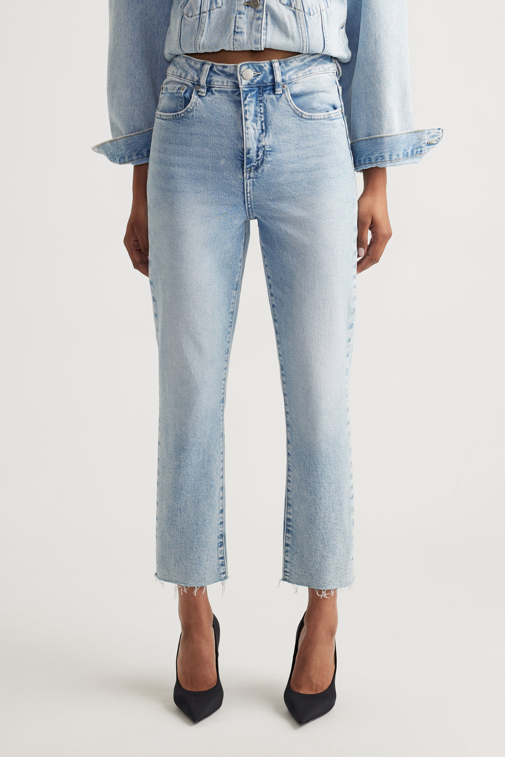 Light wash high-rise straight jeans with raw hem detail styled with a matching denim jacket and black heels.