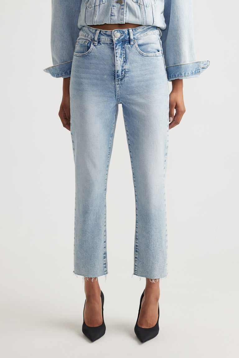 Light wash high-rise straight jeans with raw hem detail styled with a matching denim jacket and black heels.