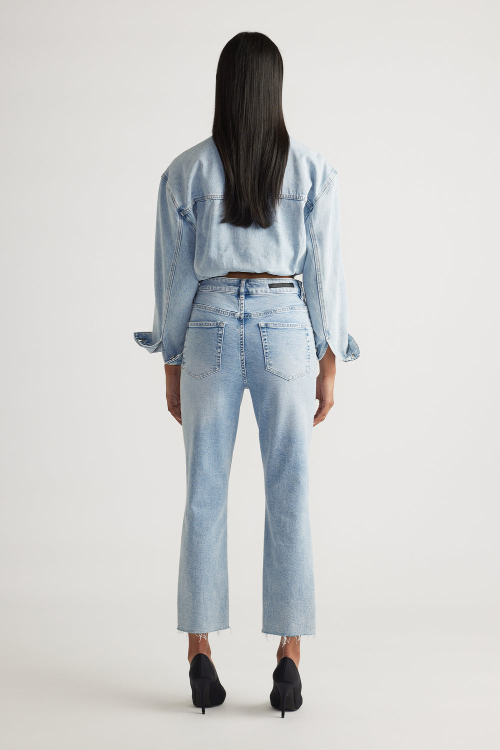 Woman seen from behind wearing light blue high-rise straight jeans paired with a matching denim jacket and black heels.