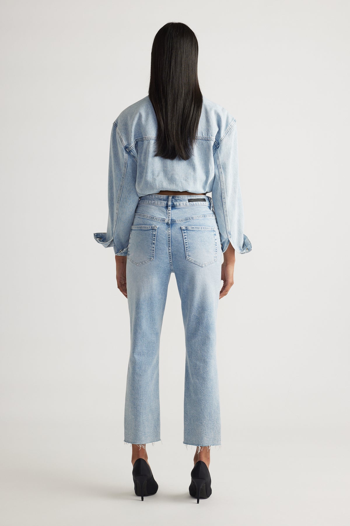 Woman seen from behind wearing light blue high-rise straight jeans paired with a matching denim jacket and black heels.