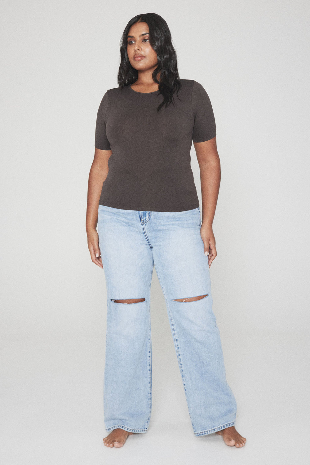 Woman wearing a fitted dark brown short sleeve tee with light blue ripped wide leg jeans