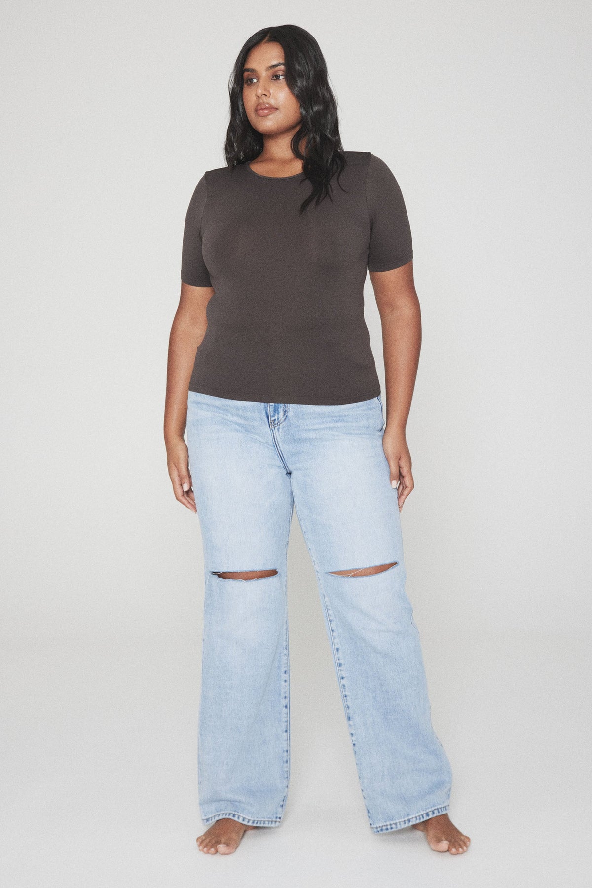 Woman wearing a fitted dark brown short sleeve tee with light blue ripped wide leg jeans