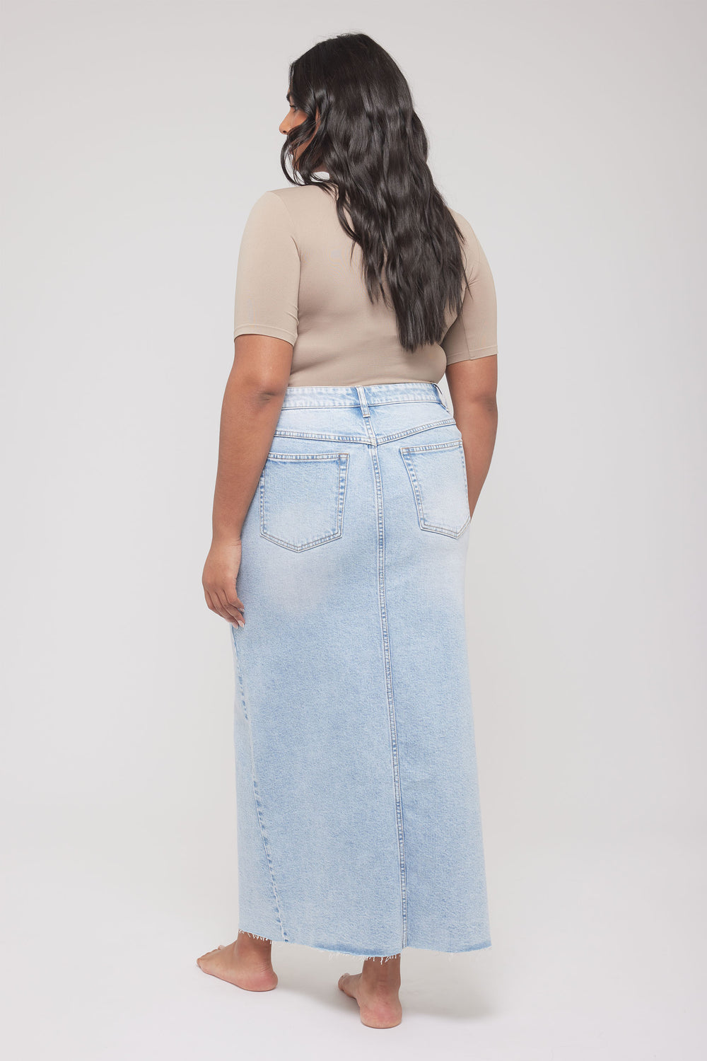 Back view of model wearing a beige fitted short sleeve tee with a long light wash denim skirt