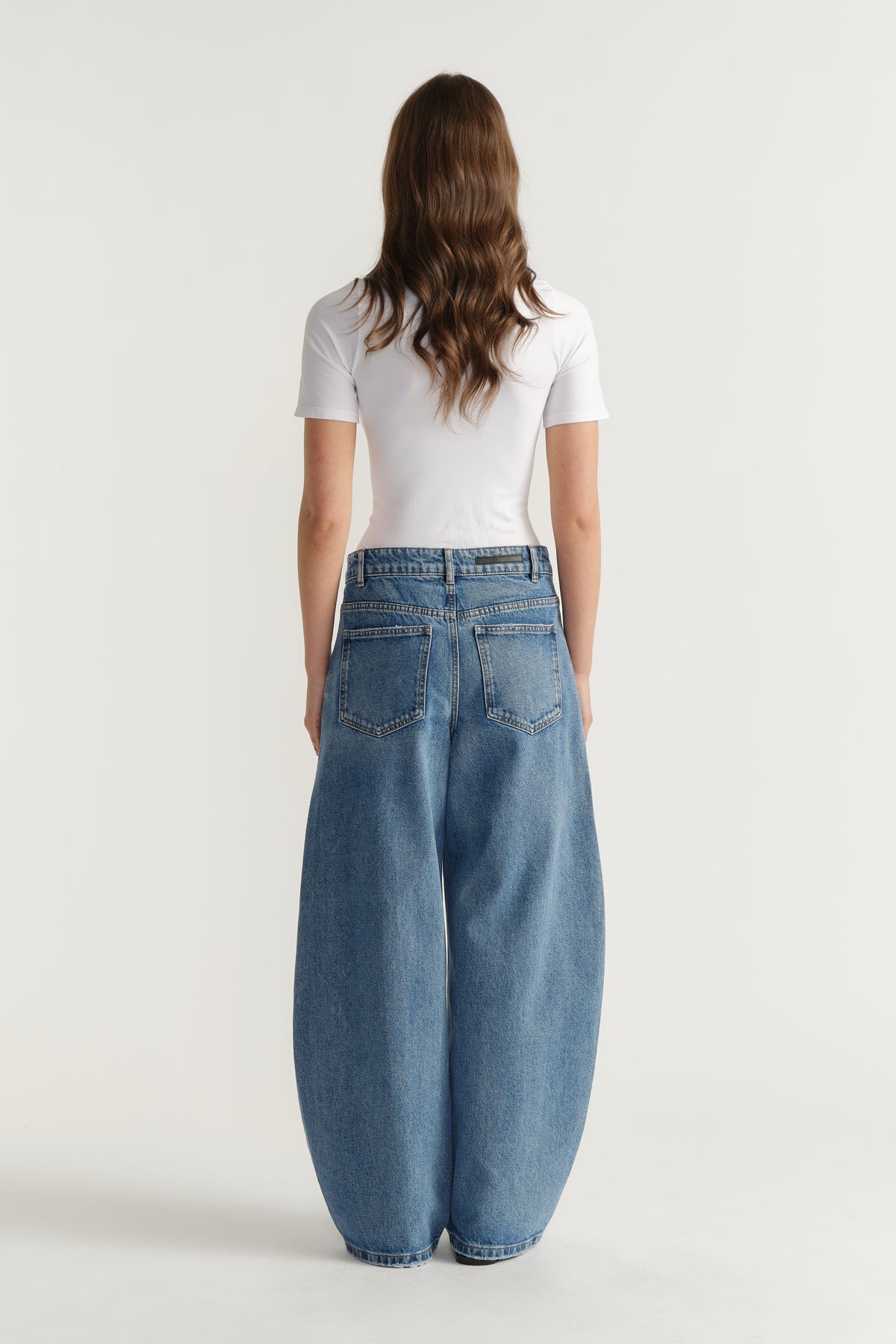 Woman seen from behind wearing a fitted white tee paired with relaxed wide-leg blue denim jeans for a casual look.