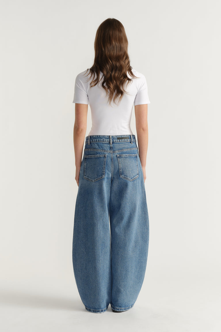 Woman seen from behind wearing a fitted white tee paired with relaxed wide-leg blue denim jeans for a casual look.