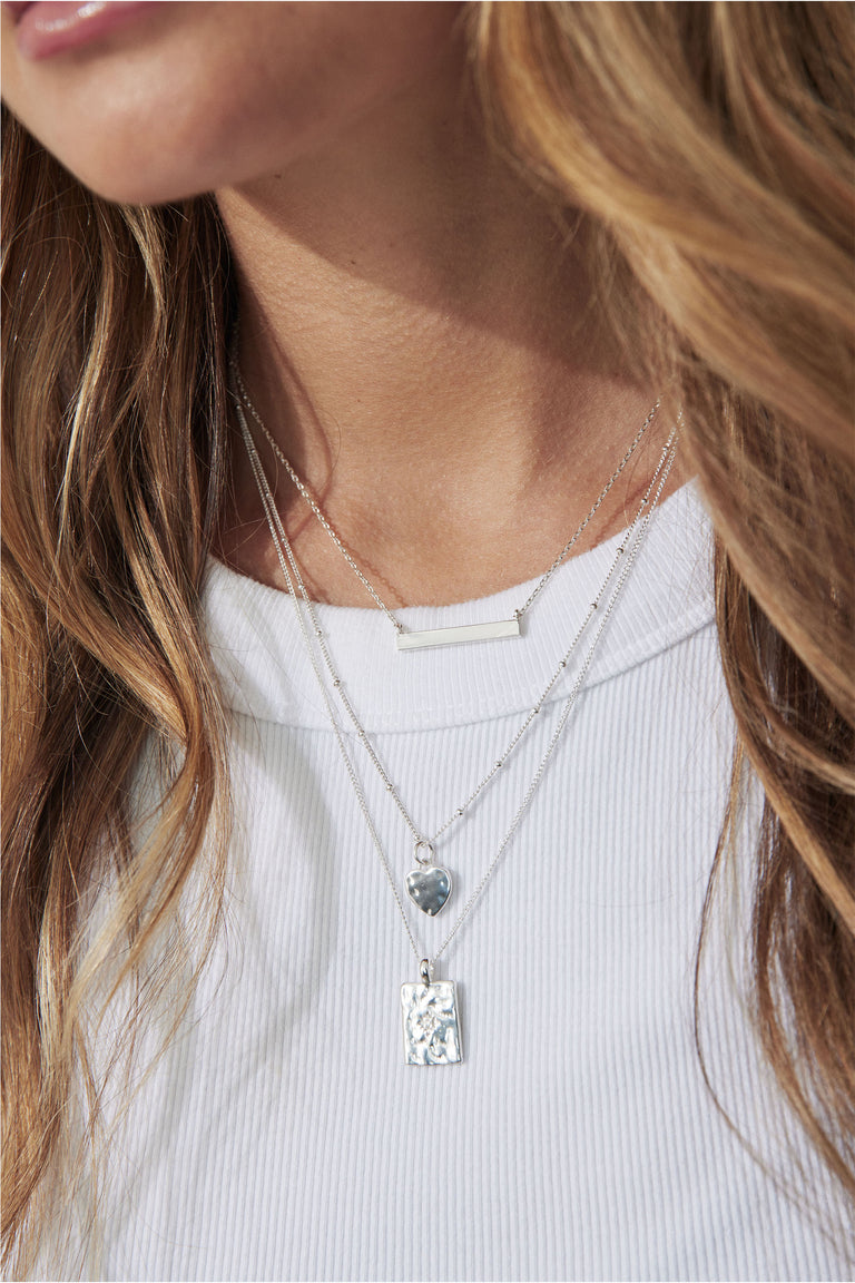 Textured plate necklace layered with pendant chains over a white ribbed top