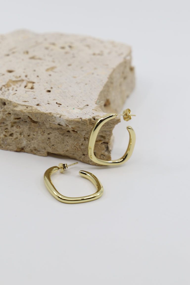 Pair of 9ct gold plated irregular hoop earrings with a smooth polished finish, displayed on textured stone.