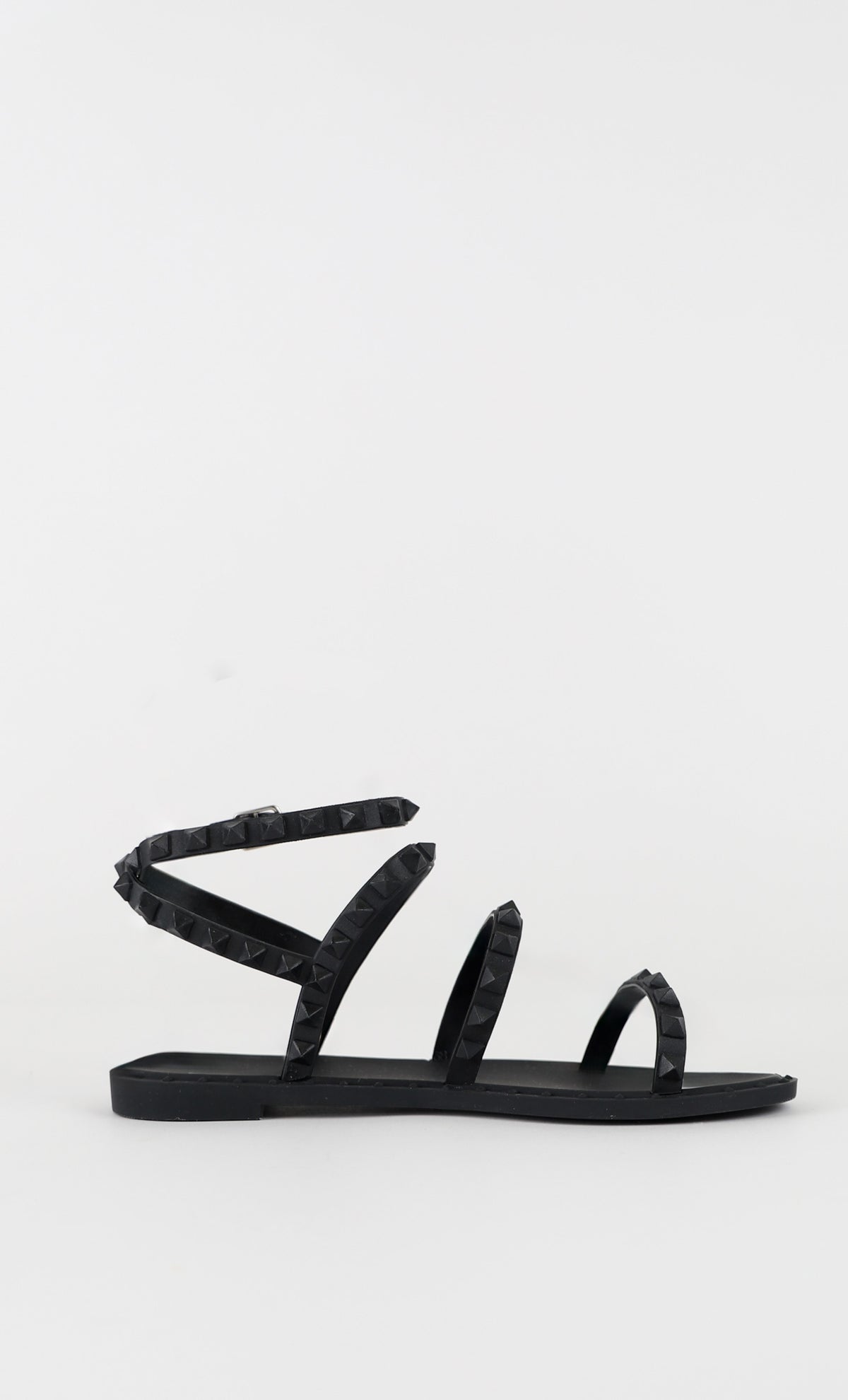 Black flat sandal with multiple studded straps and ankle wrap, featuring a minimalist and edgy summer design.