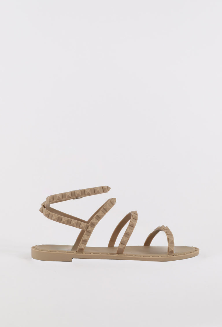 Beige flat sandal with textured straps wrapping around the ankle and minimalist open toe design for casual wear.