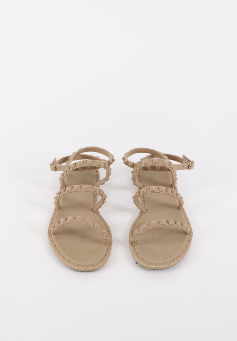 Beige flat sandals featuring studded straps with adjustable buckles for a stylish and comfortable fit.