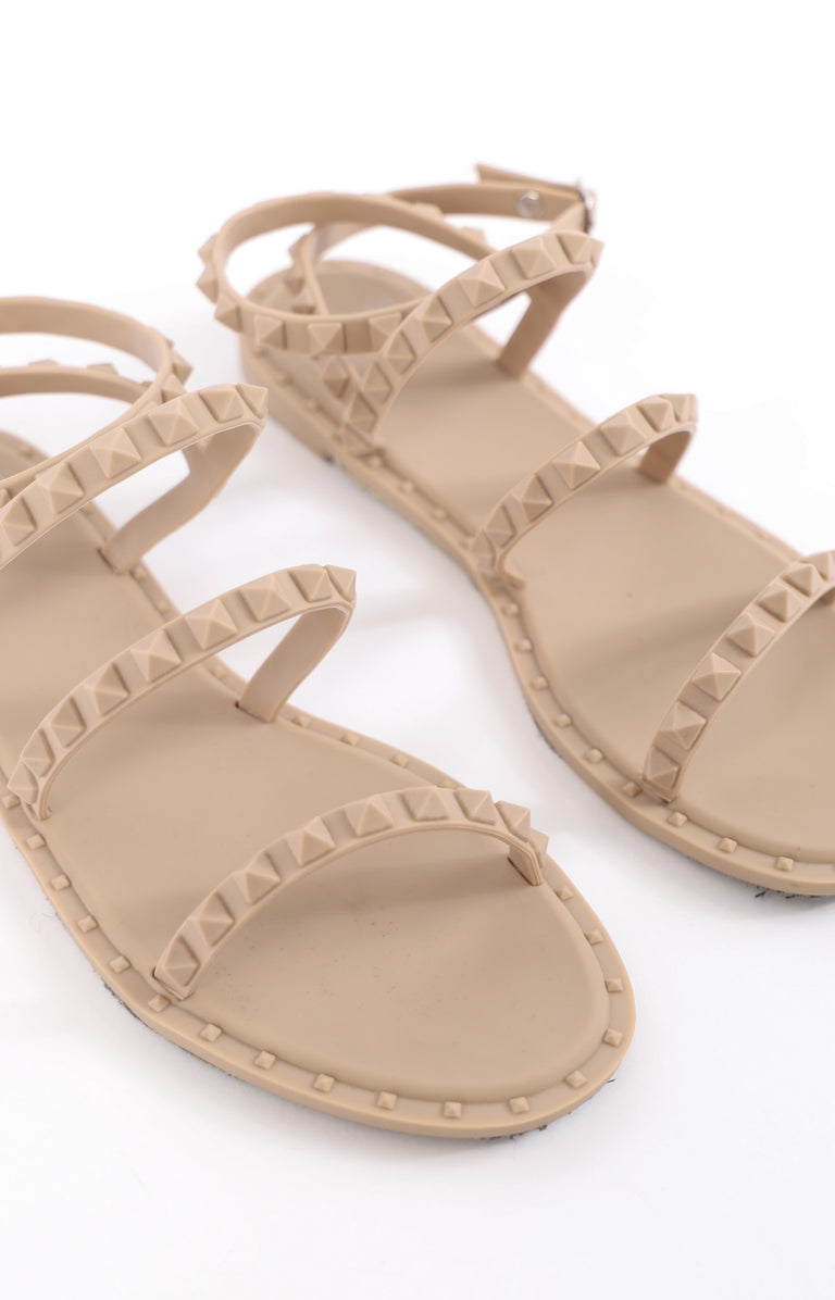 Beige flat sandals with multiple studded straps and a minimalist design for casual summer wear.