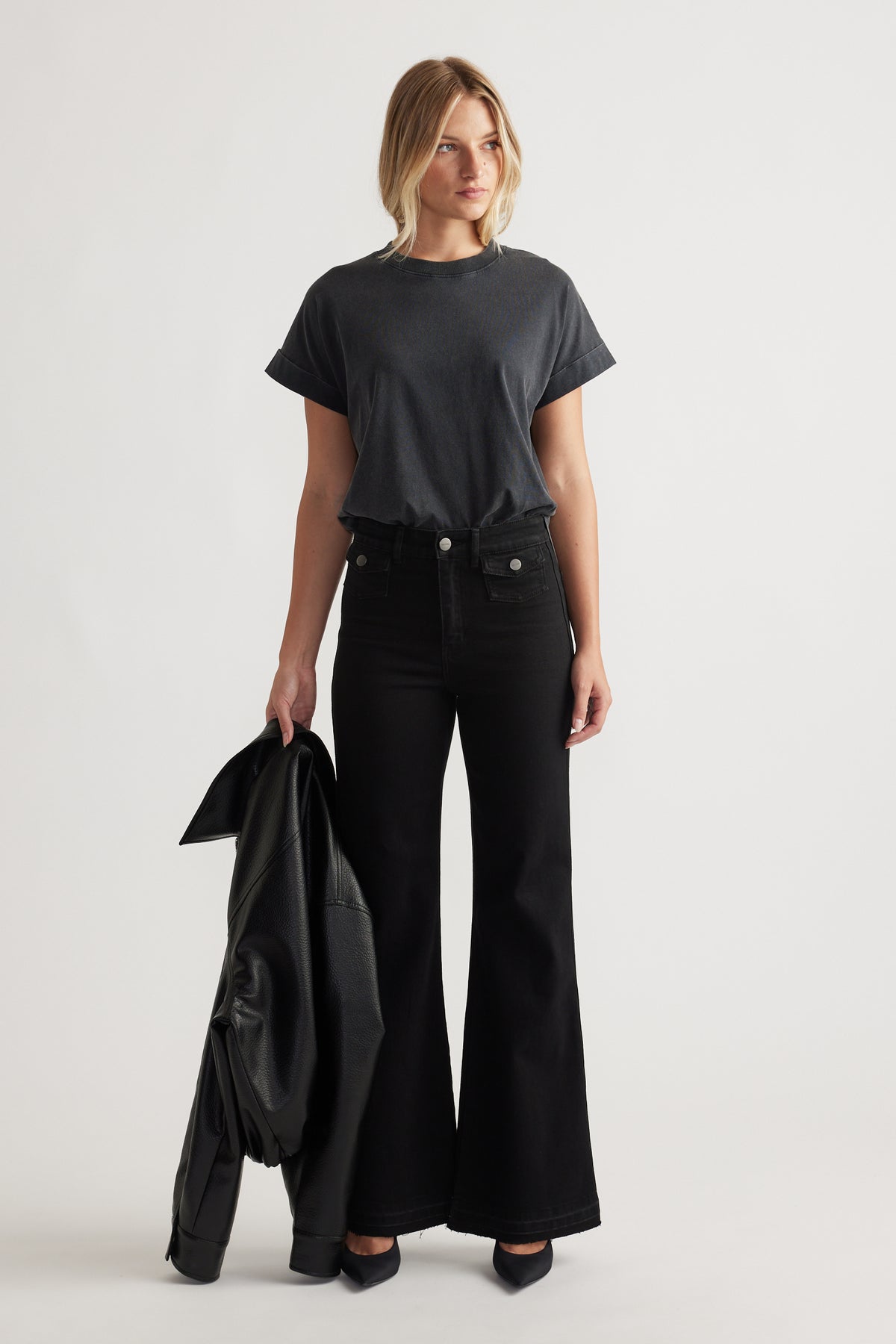 Woman wearing a black crew tee with rolled cuffs paired with high-waisted wide-leg black jeans and holding a leather jacket