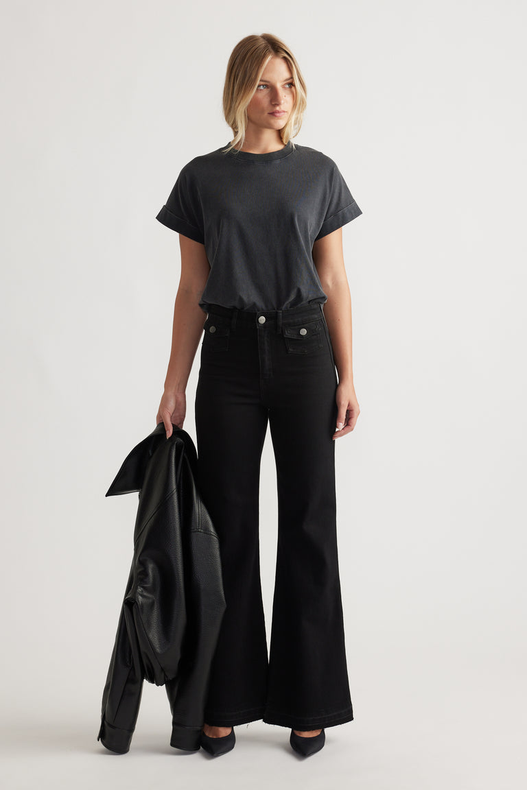 Woman wearing a black crew tee with rolled cuffs paired with high-waisted wide-leg black jeans and holding a leather jacket