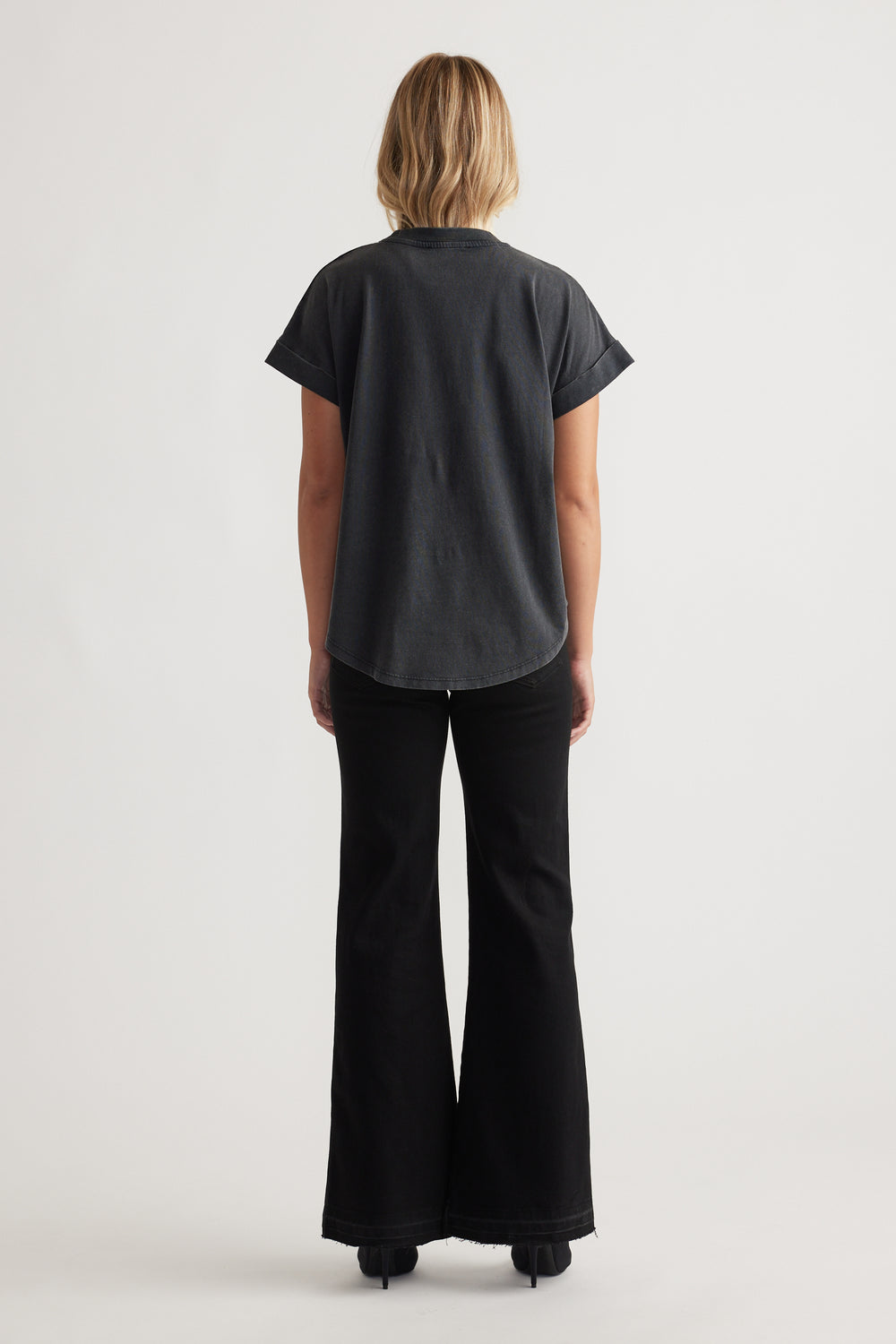 Woman seen from behind wearing a relaxed black Chloe Crew Tee with cuffed short sleeves and black flared pants for a chic vibe