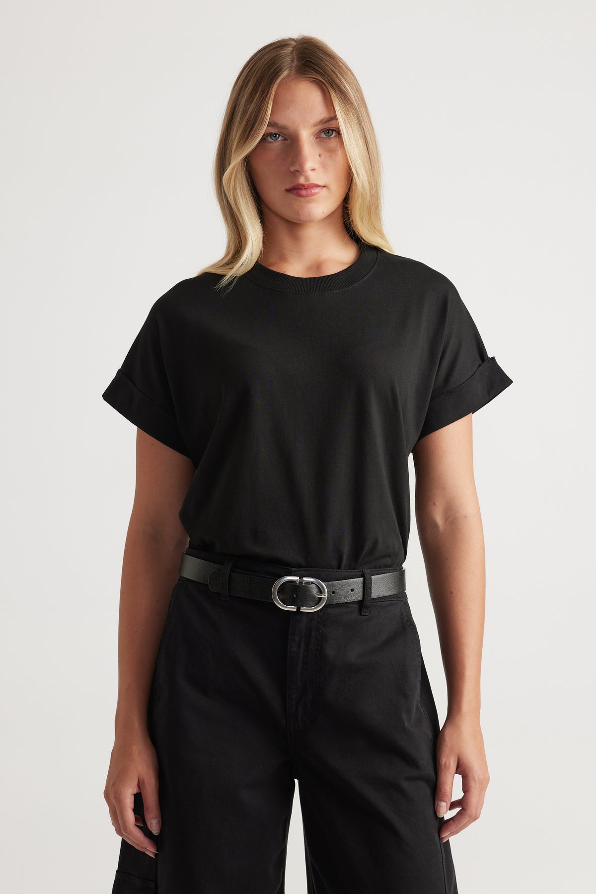 Woman wearing a relaxed black crew neck tee with rolled short sleeves and a black belt paired with dark high-waisted pants